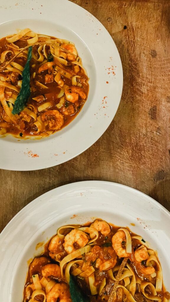 Two plates of shrimp pasta with rich tomato sauce, garnished stylishly.