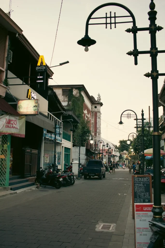 Urban street at twilight with shops, scooters, and streetlights creating a serene atmosphere.