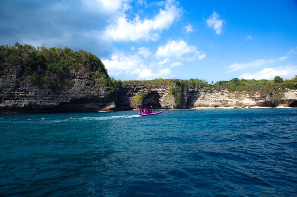 Vibrant blue ocean against dramatic cliffs in Bali, featuring a colorful boat.