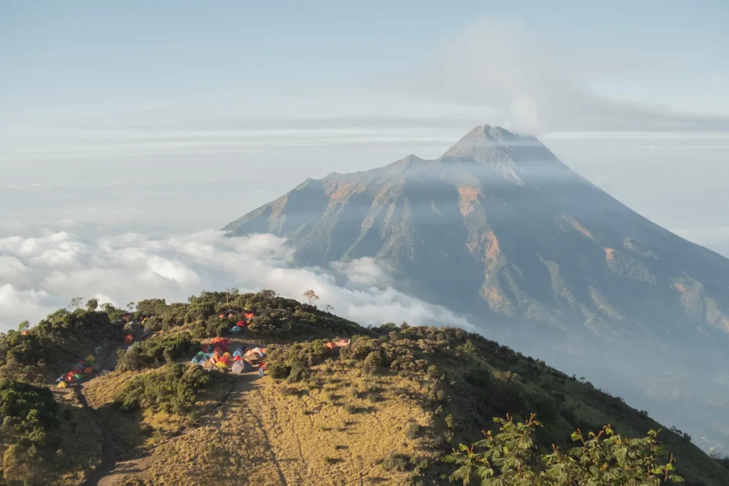 View of Mount Merapi with campsite amidst sea of clouds at sunrise.