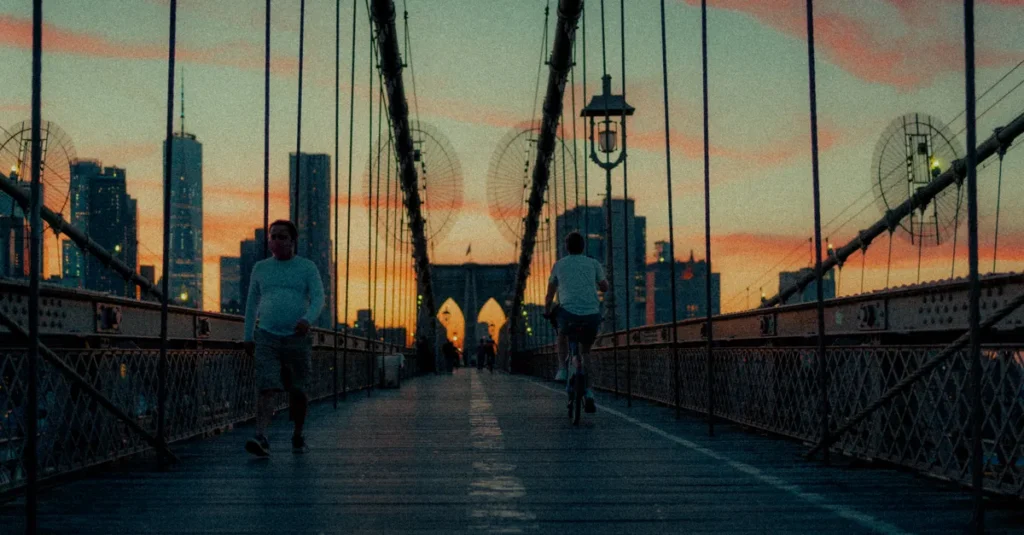 New York à deux : le guide concret pour un premier séjour (sans se laisser aspirer par la foule) View of the Brooklyn Bridge at sunset with people walking and city skyline in the background.