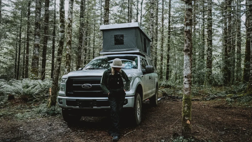 Woman camping with a tent on a pickup truck in the Oregon woods, showcasing adventure and travel lifestyle.