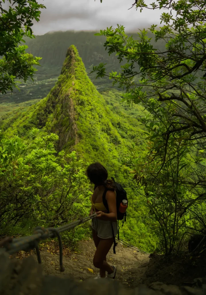 Woman hiking the steep and scenic Olomana Trail surrounded by lush greenery.