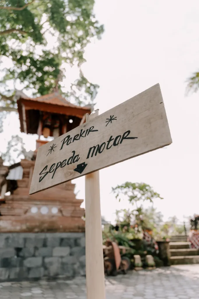 Wooden sign for motorbike parking at a Balinese temple with traditional architecture in view.