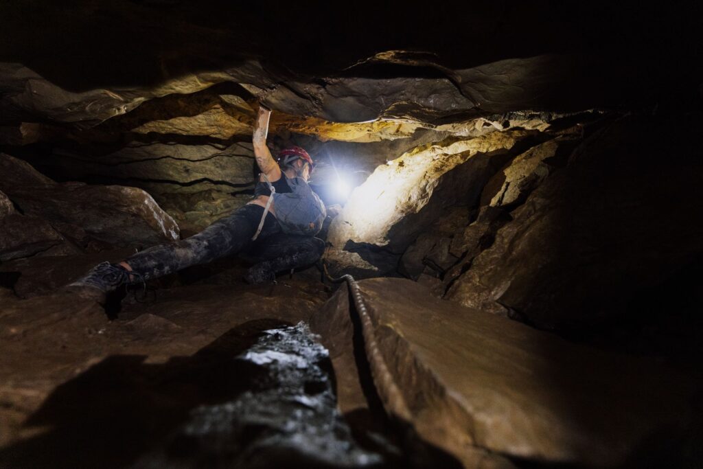 Dynamic image of a caver navigating a rocky subterranean world with headlamp illumination.