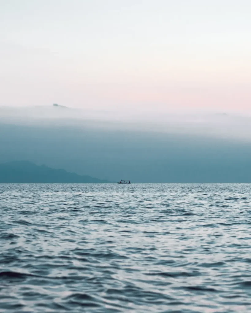 Peaceful ocean seascape with a distant boat on the horizon during sunrise, creating a calm atmosphere.