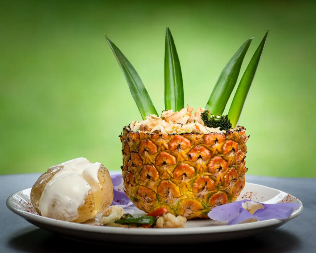 Pineapple bowl filled with rice and a baked potato served with creamy topping.