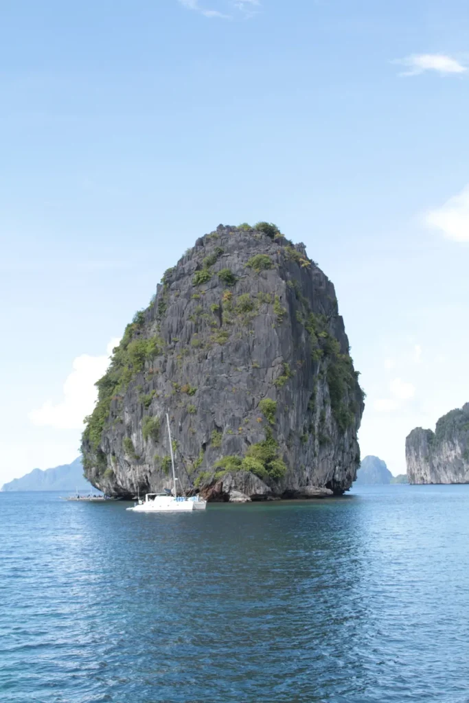 Sailboat gliding past towering limestone island in El Nido, Philippines.