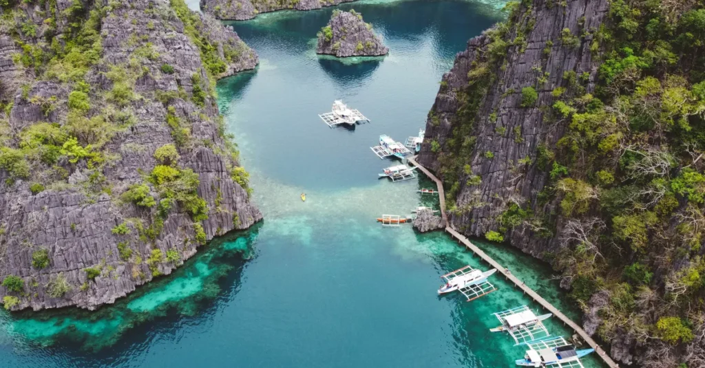 Coron à deux : le Tour A « Ultimate Coron Palawan Tour » (sans se cramer) Stunning aerial shot of boats in crystal clear waters surrounded by rocky cliffs in Coron, Philippines.